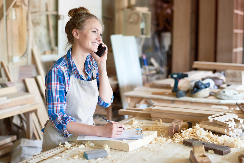 Young woman standing in a cabinetry workshop taking notes while on the phone with a customer.