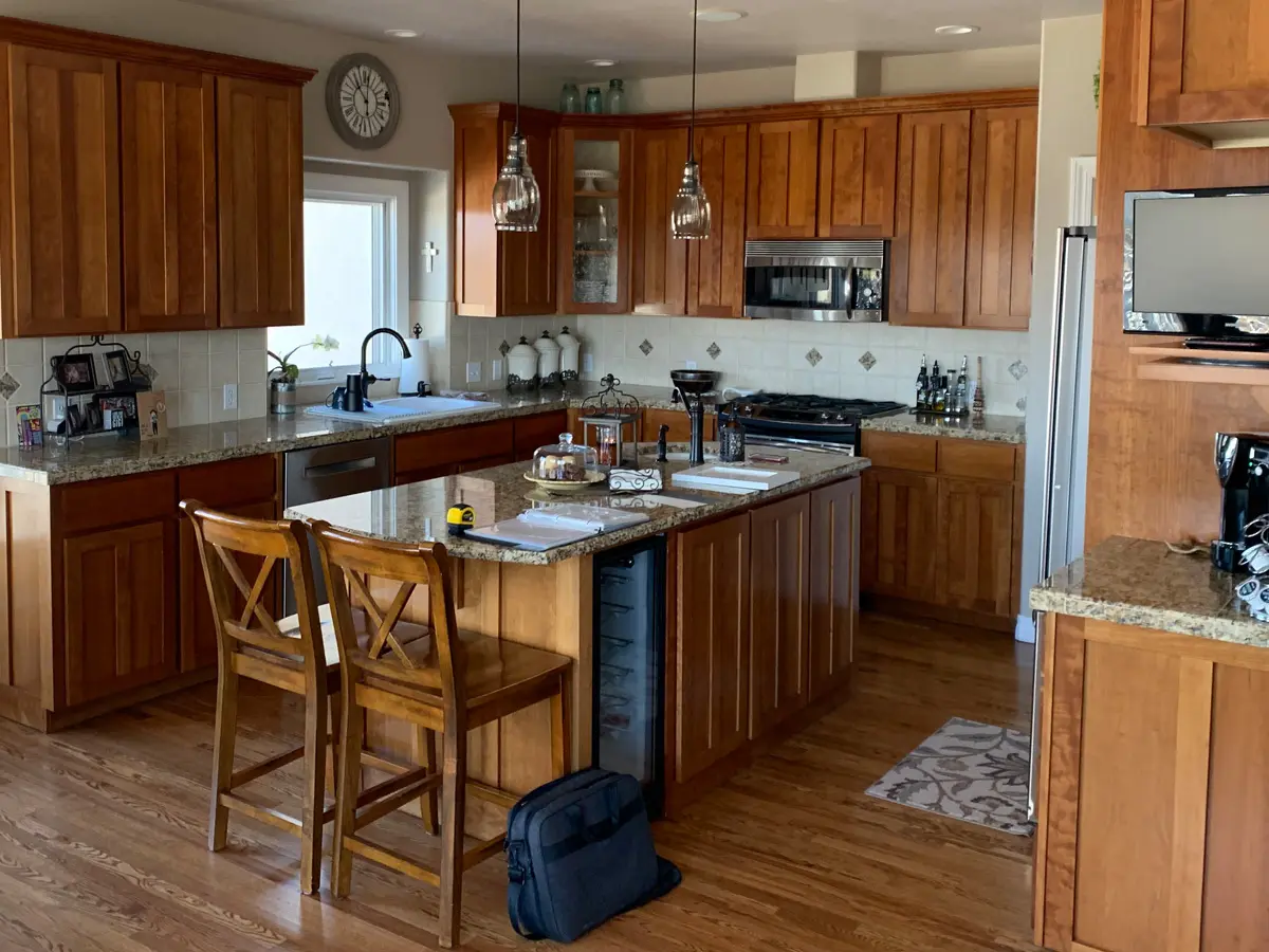 Spacious kitchen with wooden cabinets, granite countertops, and an island with bar stools. Modern appliances and pendant lighting create a warm, inviting atmosphere.