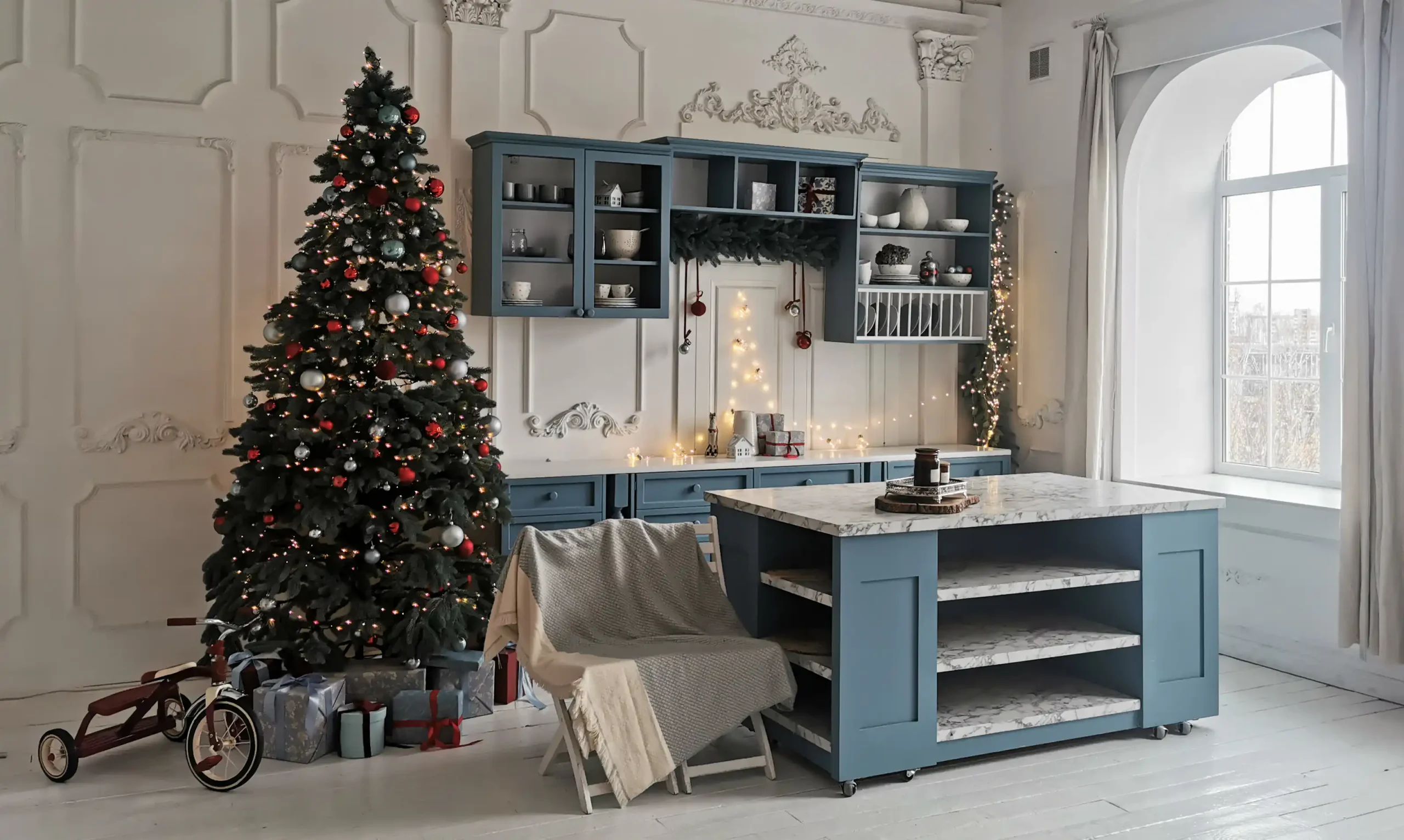 A cozy kitchen with a decorated Christmas tree, gifts, and a vintage tricycle. Blue cabinets and marble island create a festive, inviting atmosphere.