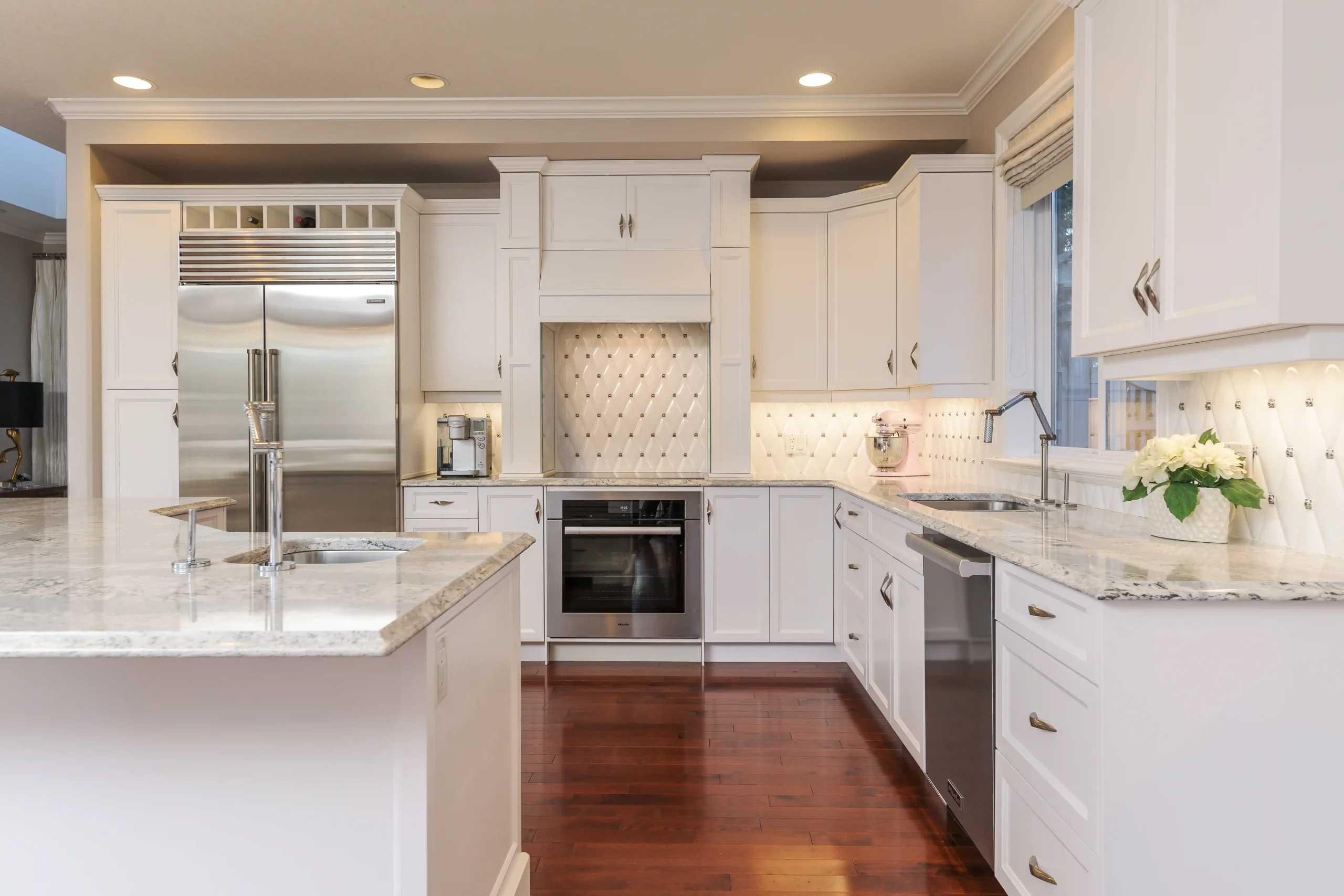 Bright, modern kitchen with white cabinets, marble countertop, stainless steel appliances, and wood flooring. Elegant backsplash and under-cabinet lighting.