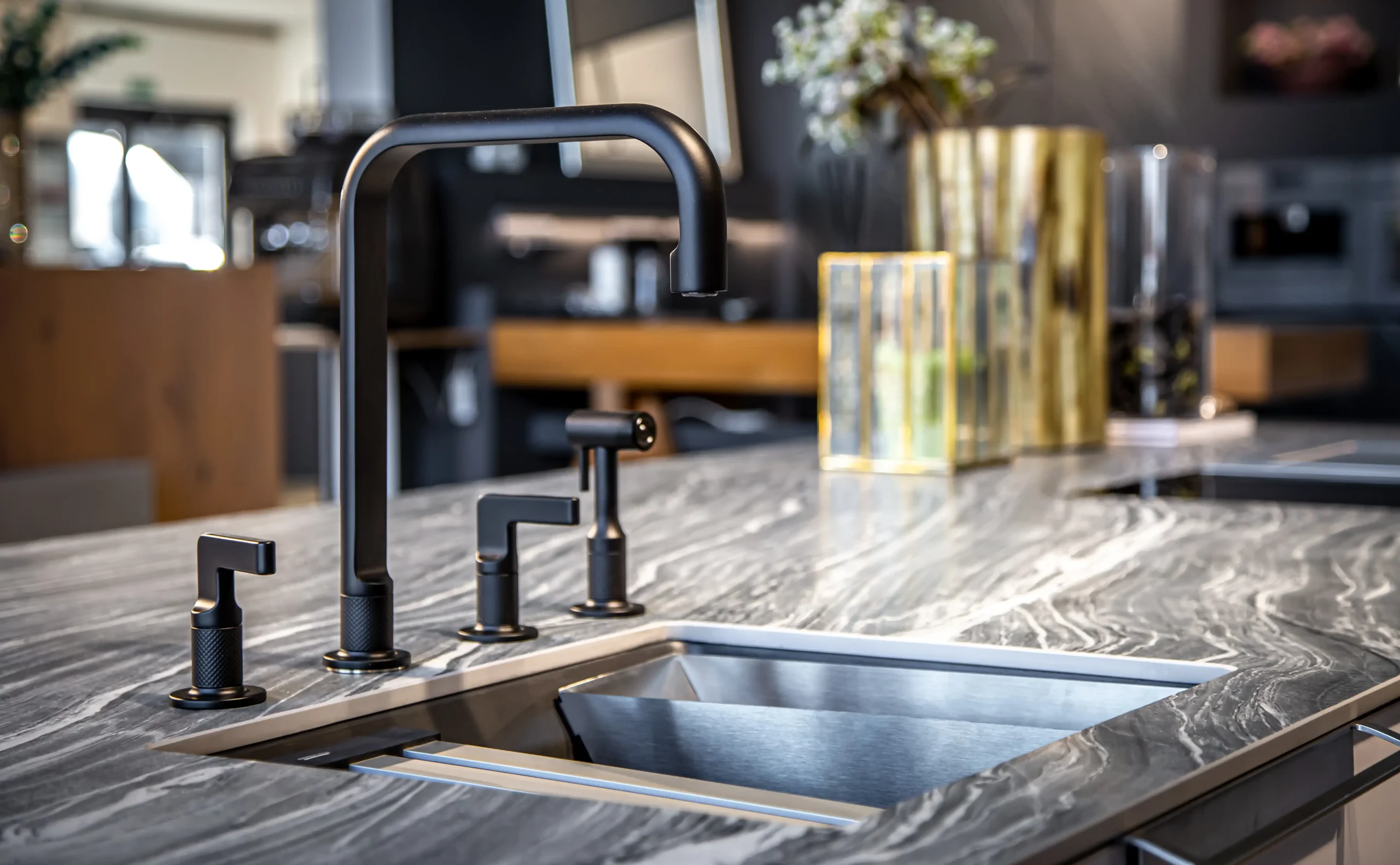 Sleek kitchen with a black faucet and modern gray marble countertop. Soft lighting, blurred background highlights gold vases and decorative elements.