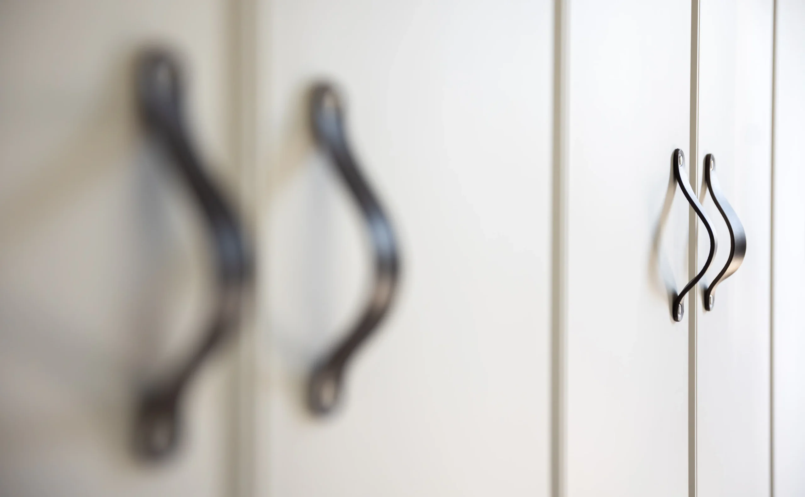 Close-up of cabinet doors with elegant black handles. The foreground handles are blurred, while the background ones are in focus, conveying a minimalist and modern feel.
