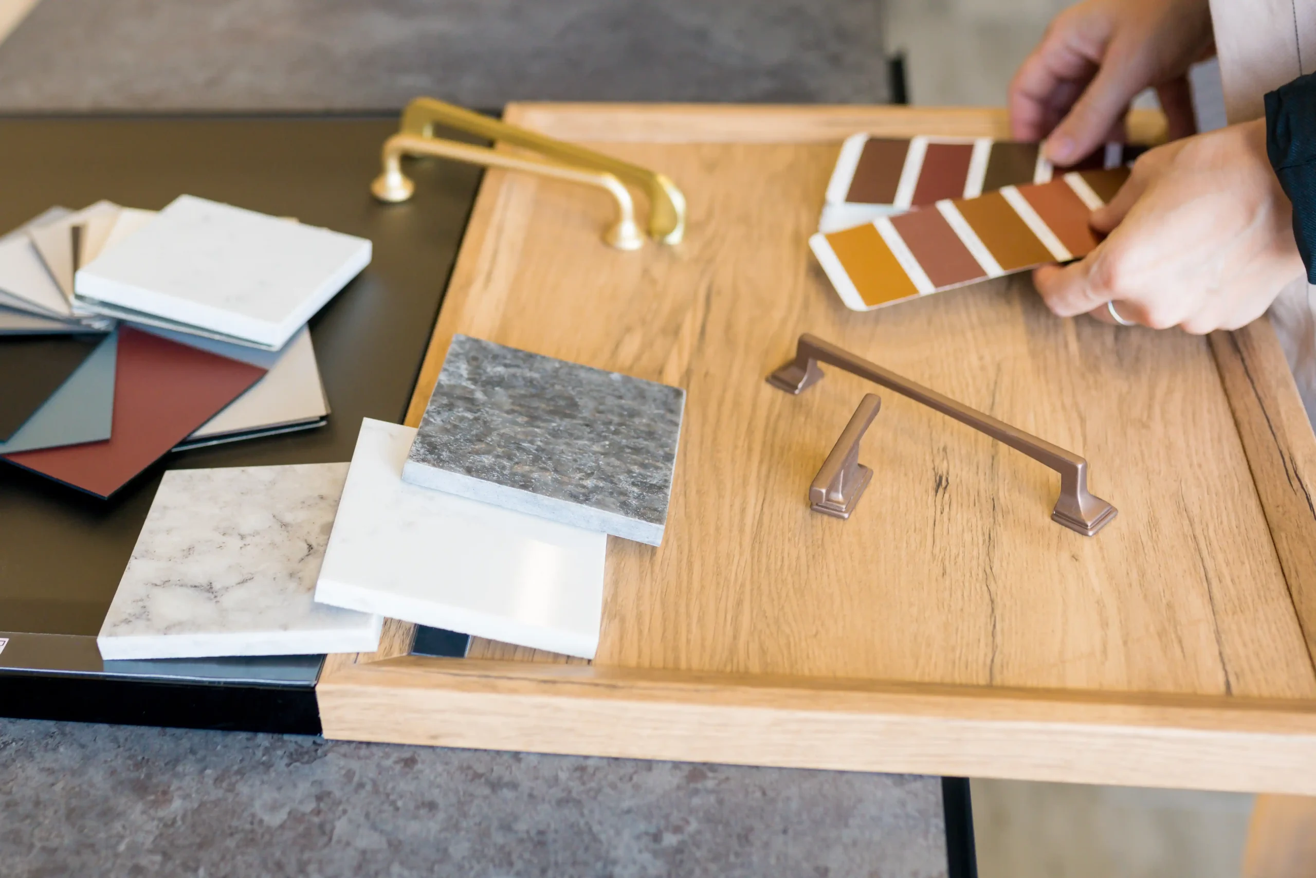 Hands sorting through wooden and metal kitchen cabinet samples and color swatches on a table, conveying a sense of design and creativity.