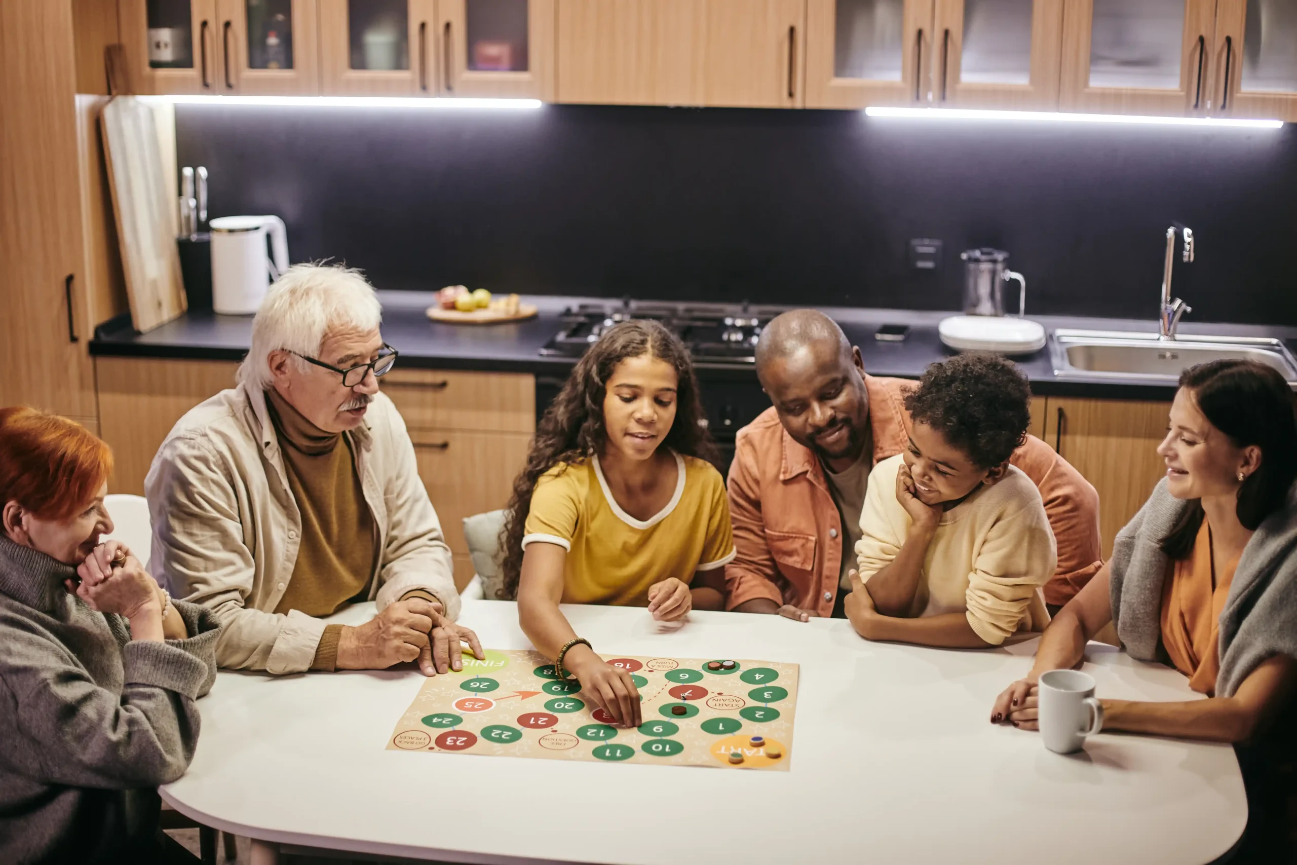 A diverse family of six gathered around a kitchen table, engaged in a board game. The atmosphere is warm and joyful, emphasizing togetherness.