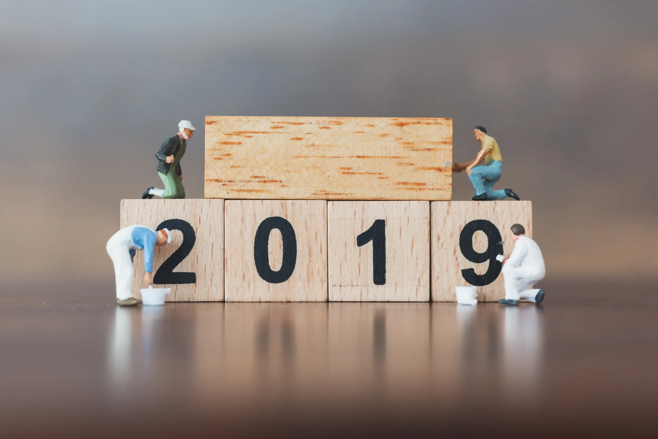 Toy figures rearranging wooden blocks display "2019" with focus on transformation. Playful, creative scene symbolizing change or progression.