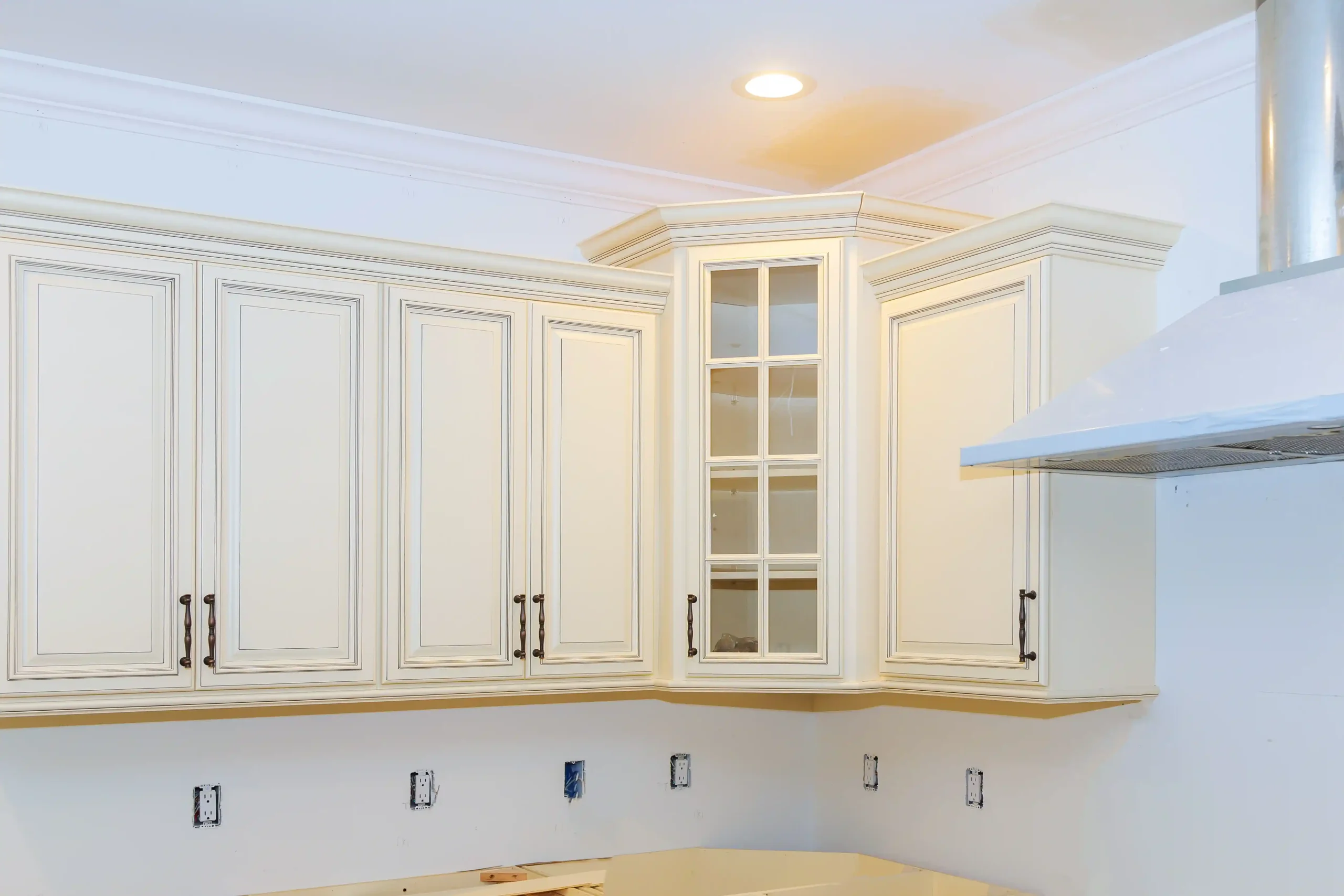 Elegant kitchen featuring cream-colored cabinets with ornate detailing and black handles, under soft recessed lighting, evoking a clean, classic atmosphere.