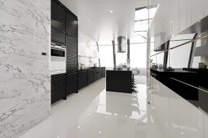 Sleek modern kitchen with glossy white floors, black cabinetry, and marble walls. Island with bar stools under skylights, creating an airy ambiance.