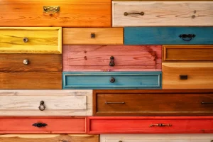 A colorful collage of various wooden drawers, each with unique handles, arranged in a grid. The drawers are painted in vibrant shades like yellow, blue, red, and orange, creating a lively and artistic pattern.