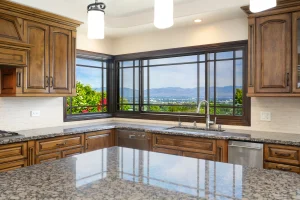 Spacious kitchen with wooden cabinets, granite countertops, and a large window with a scenic mountain view. Bright pendant lights illuminate the area.