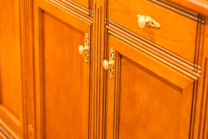 Survive a Kitchen Remodel by Refinishing Cabinets Instead Close-up of elegant wooden cabinet doors with intricate carvings and ornate metal handles, showcasing craftsmanship and a warm, classic aesthetic.